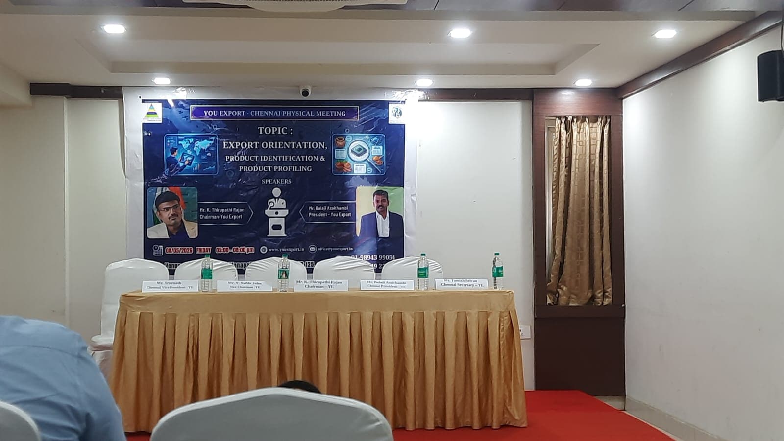 Stage backdrop and dais at the YouExport Chennai Physical Meeting on Export Orientation, Product Identification & Product Profiling — Kuber Inn Elite, Manapakkam, 8 May 2026. Banner shows the event topic with portraits of the two speakers: Mr. K. Thirupathi Rajan, Chairman of YouExport, and Mr. Balaji Asaithambi, President of YouExport.
